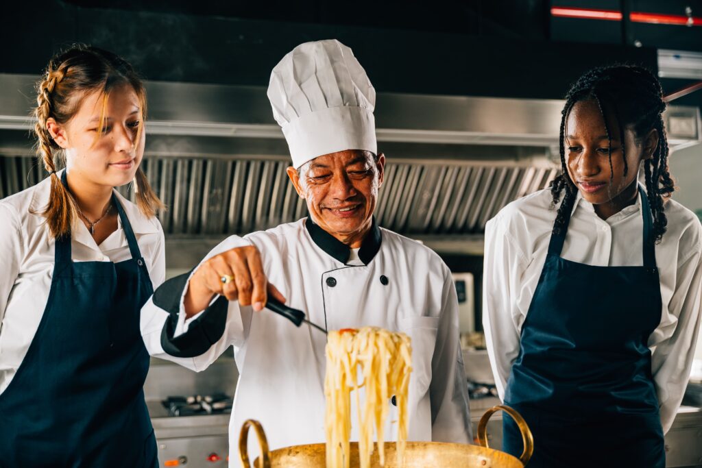 Chef mentoring two culinary students while cooking pasta