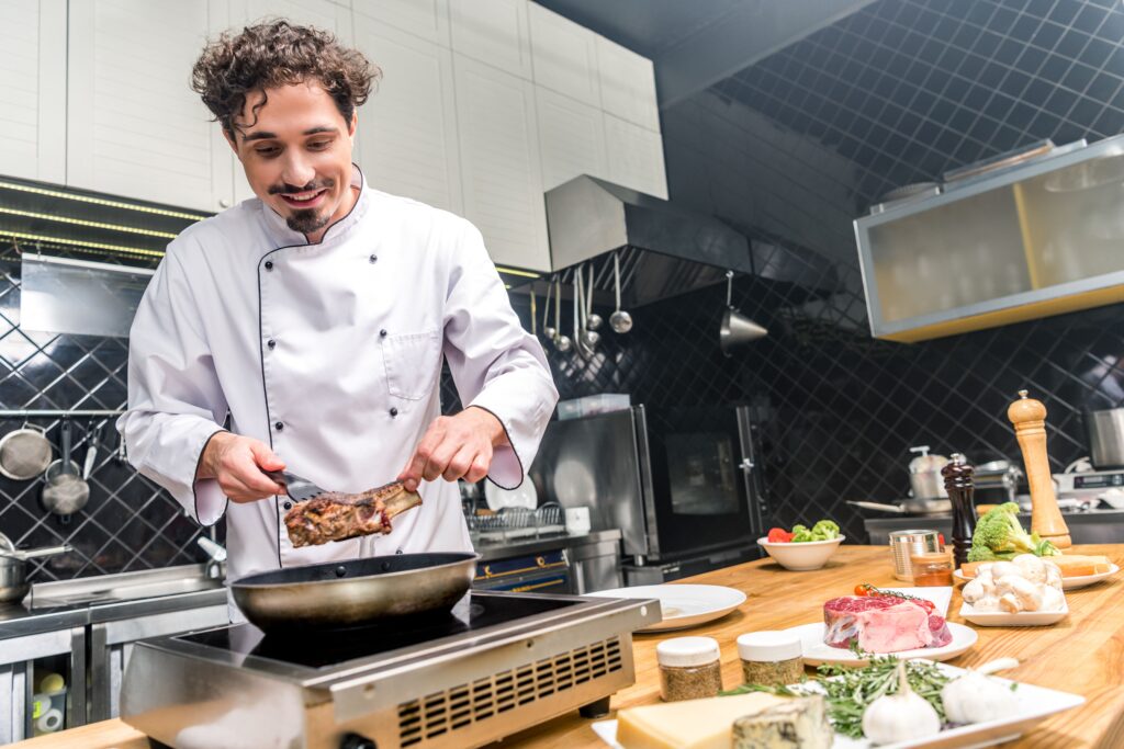 Smiling chef frying meat in a restaurant kitchen